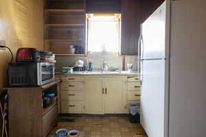Kitchen featuring freestanding refrigerator, light flooring, light countertops, open shelves, and backsplash
