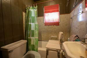 Full bath with shower / bath combo with shower curtain and wooden walls