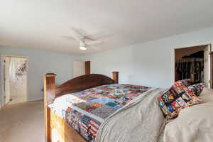 Carpeted bedroom with ceiling fan, a walk in closet, and ensuite bathroom