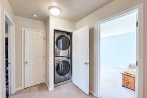 Laundry area with light colored carpet and stacked washer / dryer