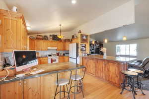 Kitchen with a peninsula, a kitchen breakfast bar, vaulted ceiling, backsplash, and pendant lighting