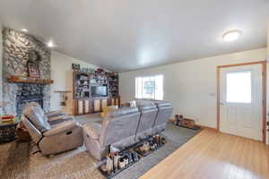 Living area featuring vaulted ceiling, light wood-type flooring, and a stone fireplace