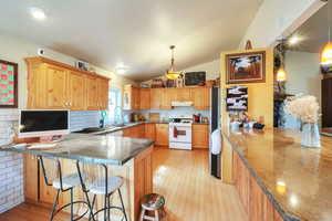 Kitchen featuring a peninsula, white stove, decorative backsplash, decorative light fixtures, and a breakfast bar