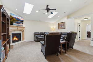 Home theater featuring lofted ceiling, a skylight, light carpet, a high end fireplace, and a ceiling fan