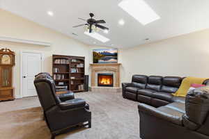 Carpeted living area featuring a skylight, vaulted ceiling, a tiled fireplace, ceiling fan, and recessed lighting