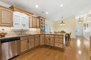 Kitchen with stainless steel dishwasher, healthy amount of natural light, light wood-style flooring, light stone countertops, and lofted ceiling