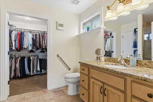 Bathroom with a walk in closet, vanity, and light colored carpet