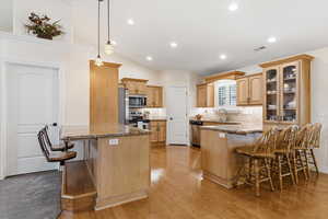 Kitchen with a breakfast bar area, a peninsula, dark stone counters, glass insert cabinets, and vaulted ceiling