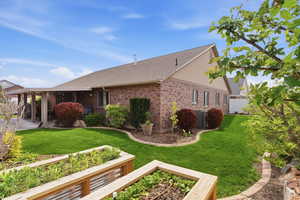 View of side of home with roof with shingles, a patio area, brick siding, and a garden
