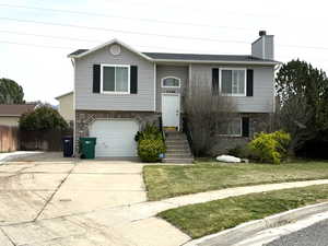 Raised ranch featuring brick siding, a garage, a chimney, and a front yard