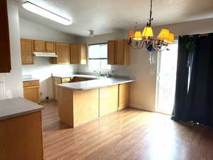 Kitchen featuring a peninsula, suspended lighting, light countertops, and light wood finished floors