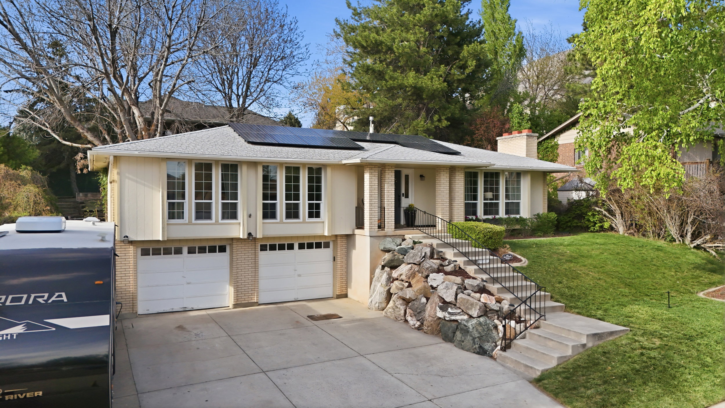 Ranch-style home featuring brick siding, roof mounted solar panels, a garage, a front yard, and driveway