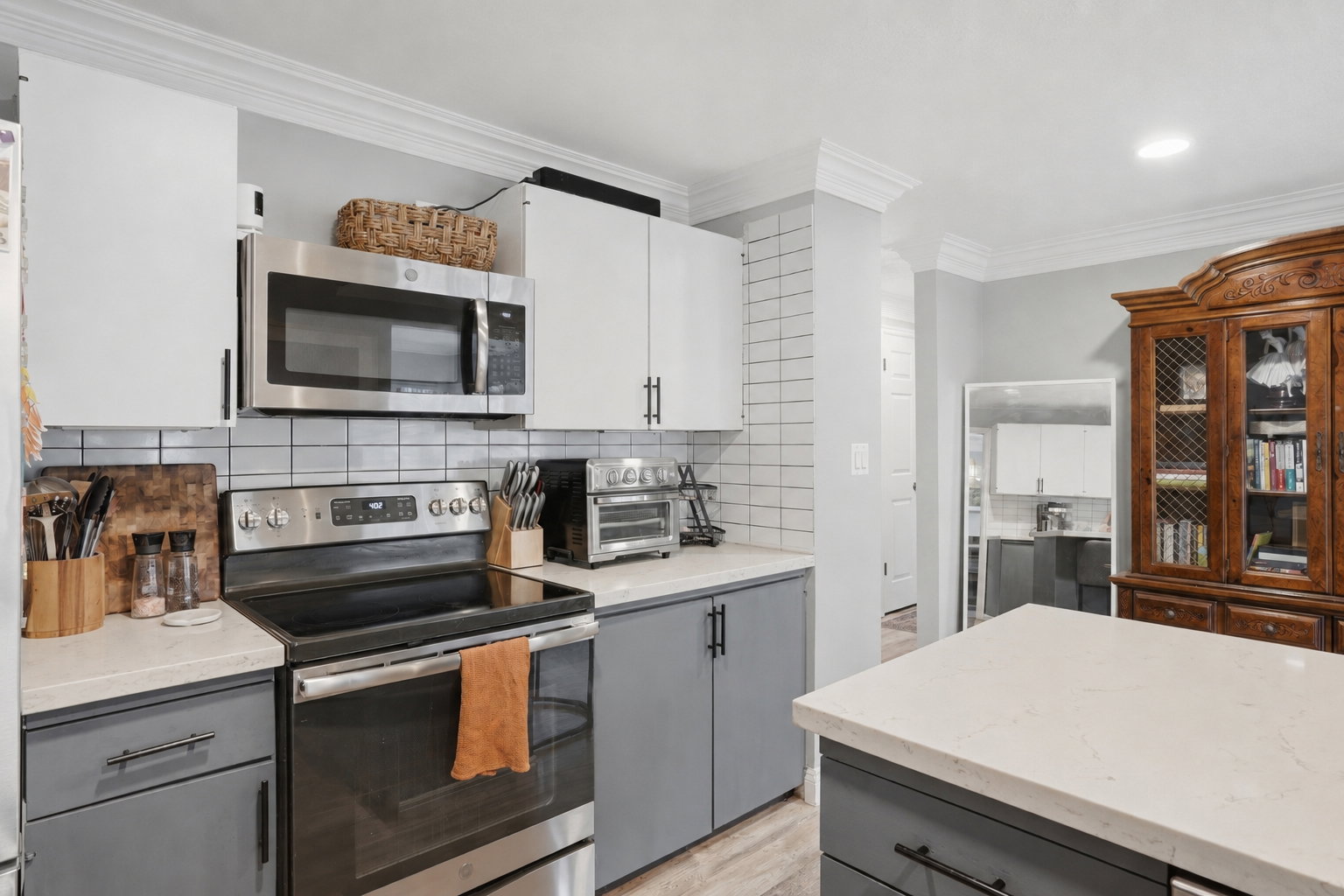 Kitchen featuring two-tone cabinetry with white upper and gray lower cabinets, light-toned countertops, and a white subway tile backsplash