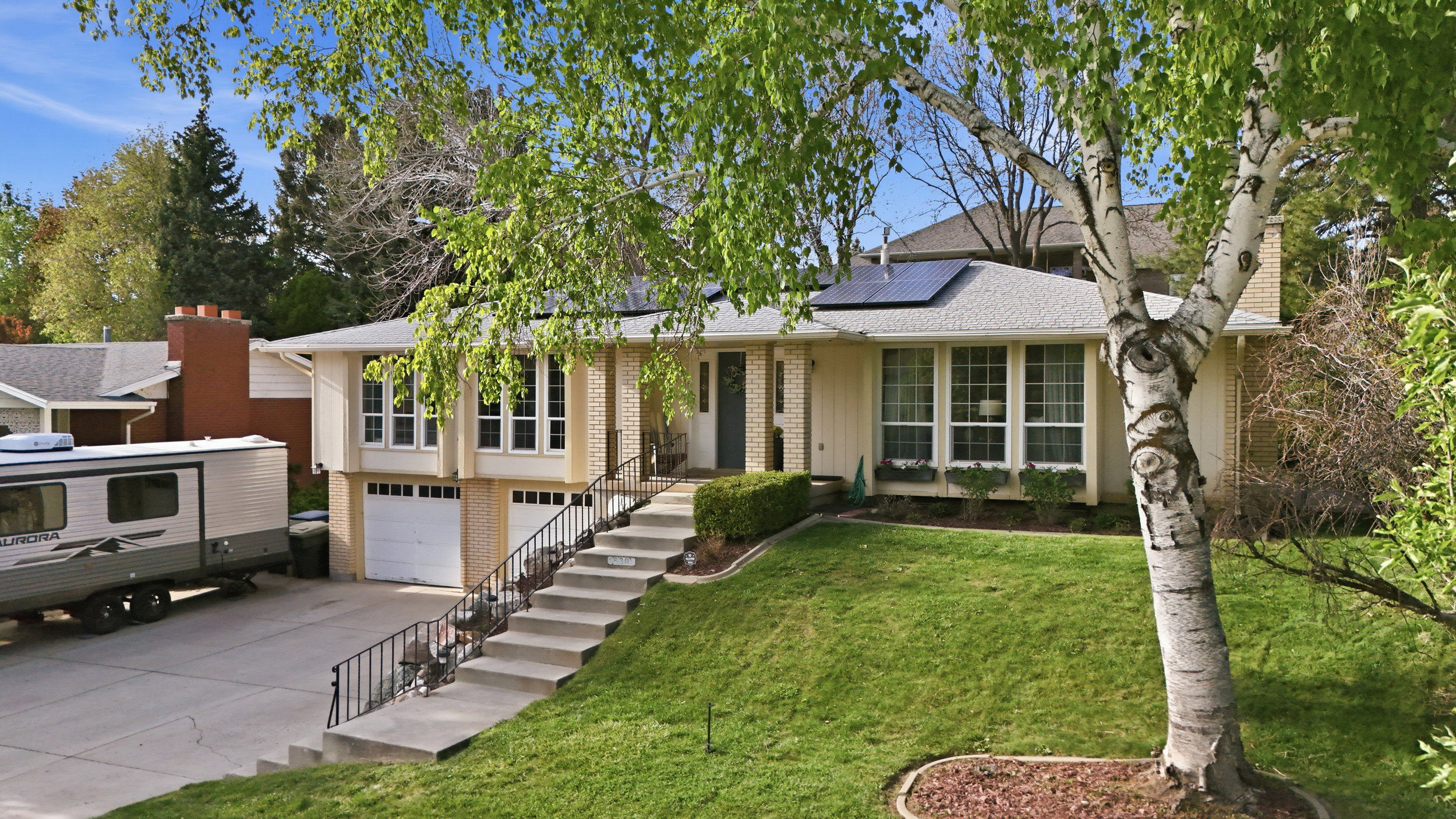 View of front of house featuring solar panels, driveway, a front yard, an attached garage, and brick siding