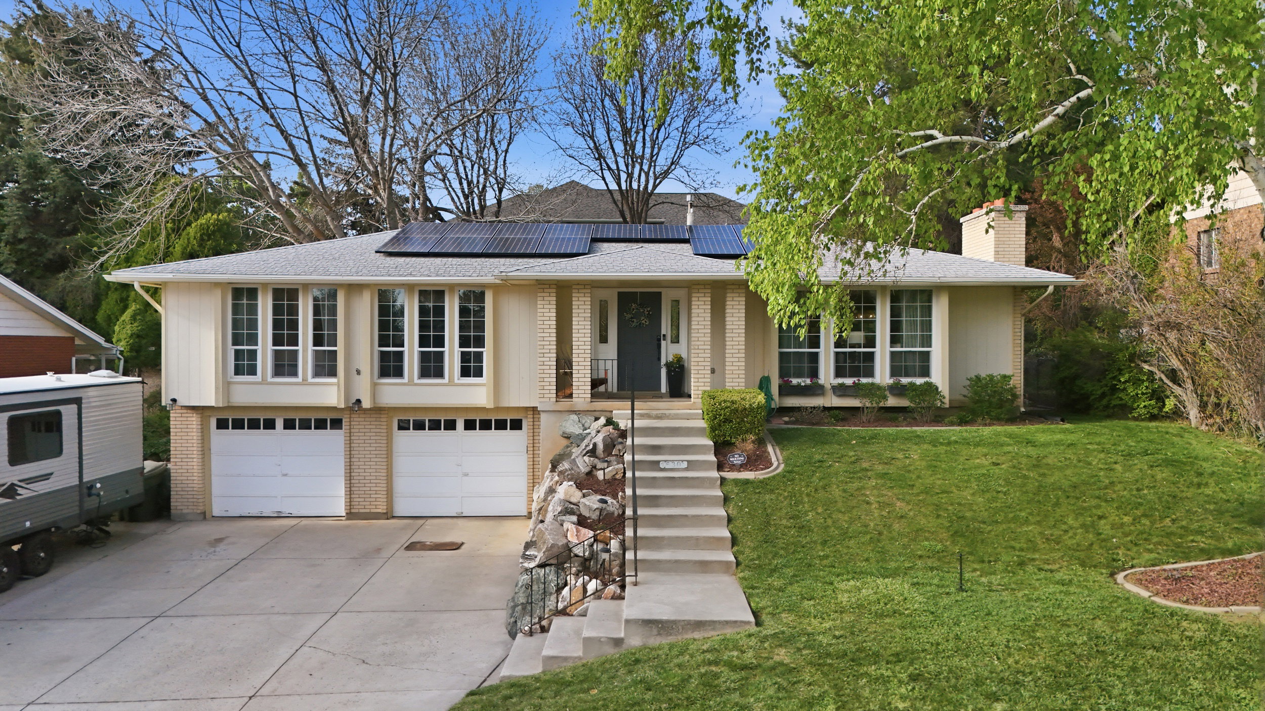Ranch-style home featuring brick siding, roof mounted solar panels, an attached garage, concrete driveway, and a front lawn
