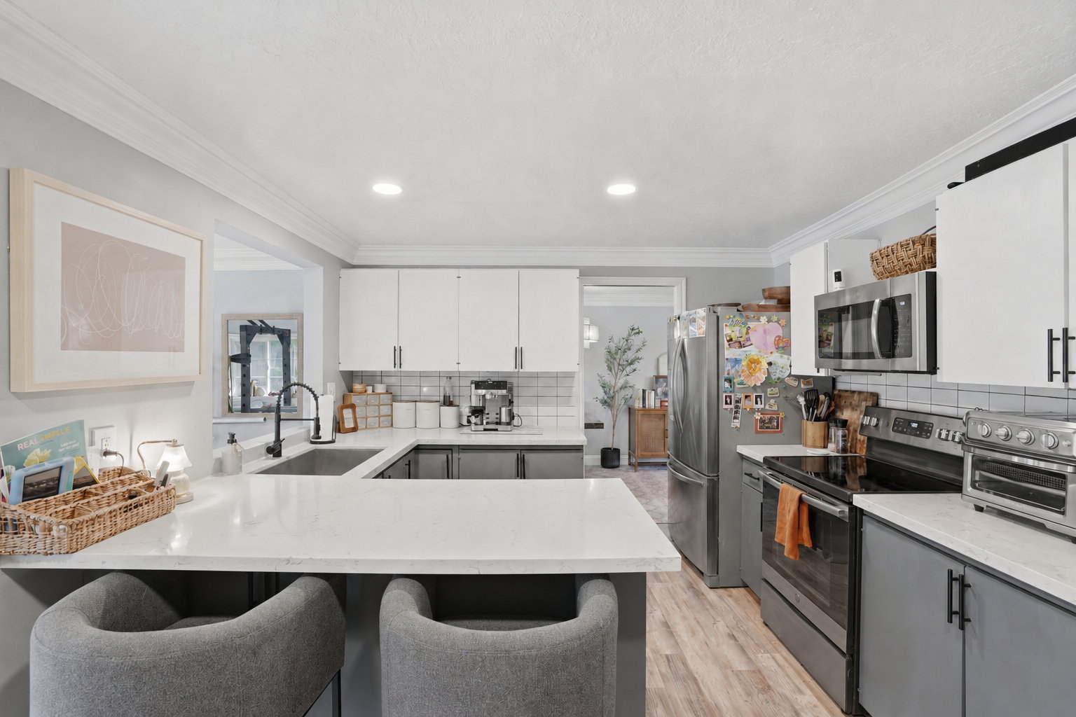 Contemporary kitchen featuring white upper cabinetry, grey lower cabinetry, stainless steel appliances, a bar-height countertop, and wood-finish flooring