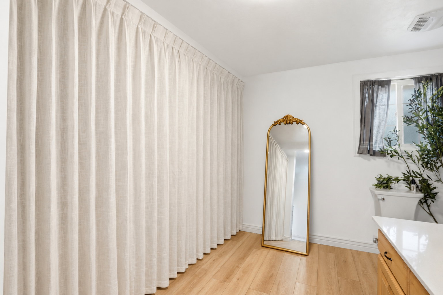 Full-length drapery paneling with blonde wood-finish flooring, a white window frame, and a built-in countertop with wood cabinetry