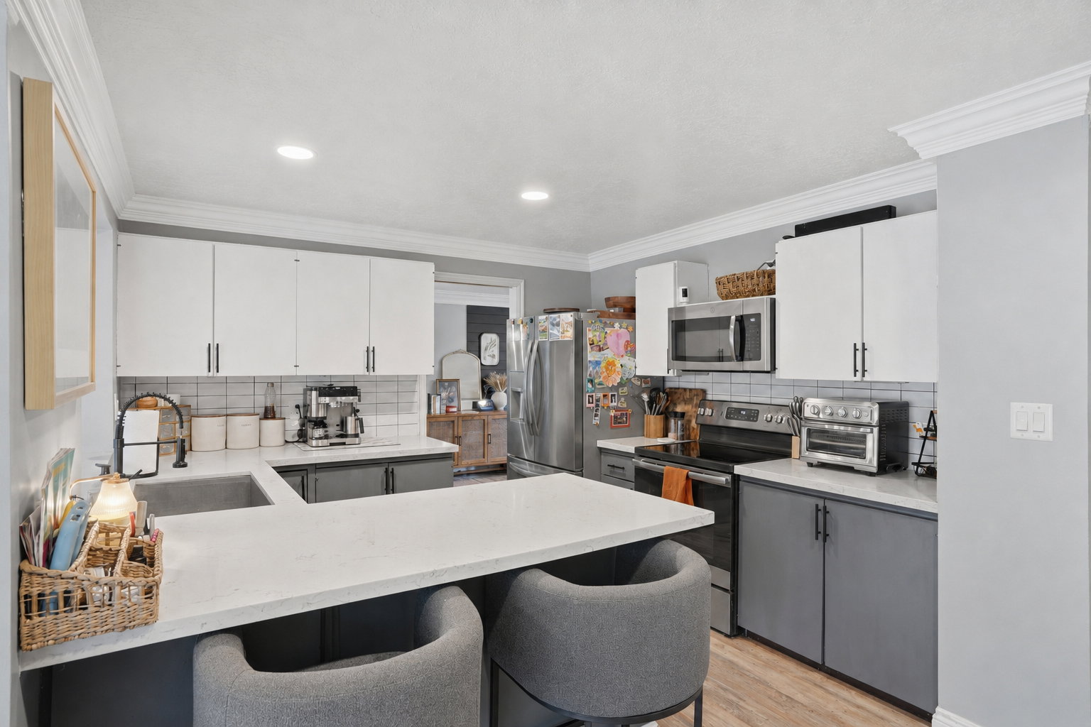 Modern kitchen featuring two-tone cabinetry with white upper and dark gray lower cabinets, a white subway tile backsplash, and a light-toned countertop with an integrated sink