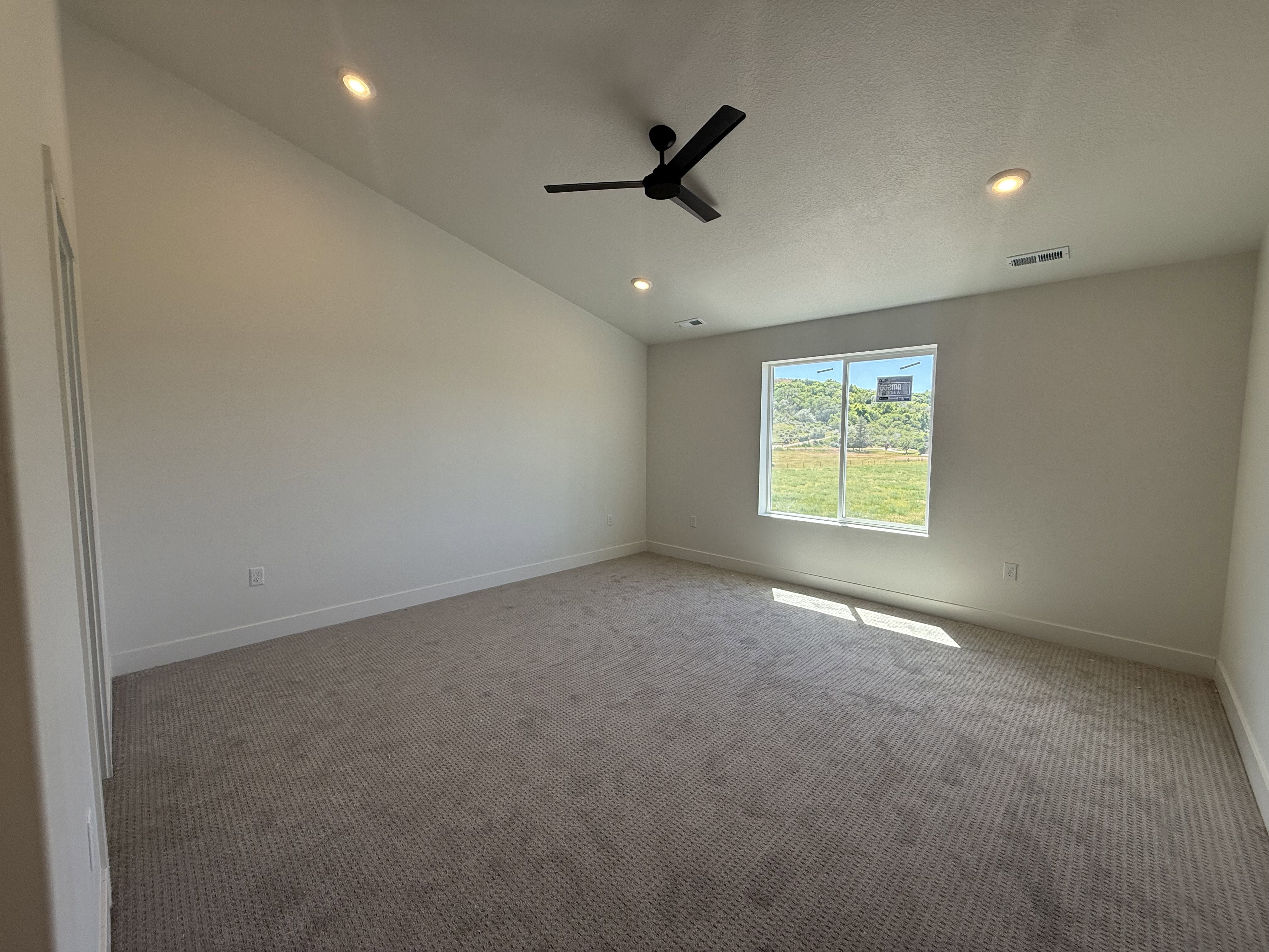 Spacious room featuring vaulted ceilings, recessed lighting, a modern ceiling fan, wall-to-wall carpeting, and a large window