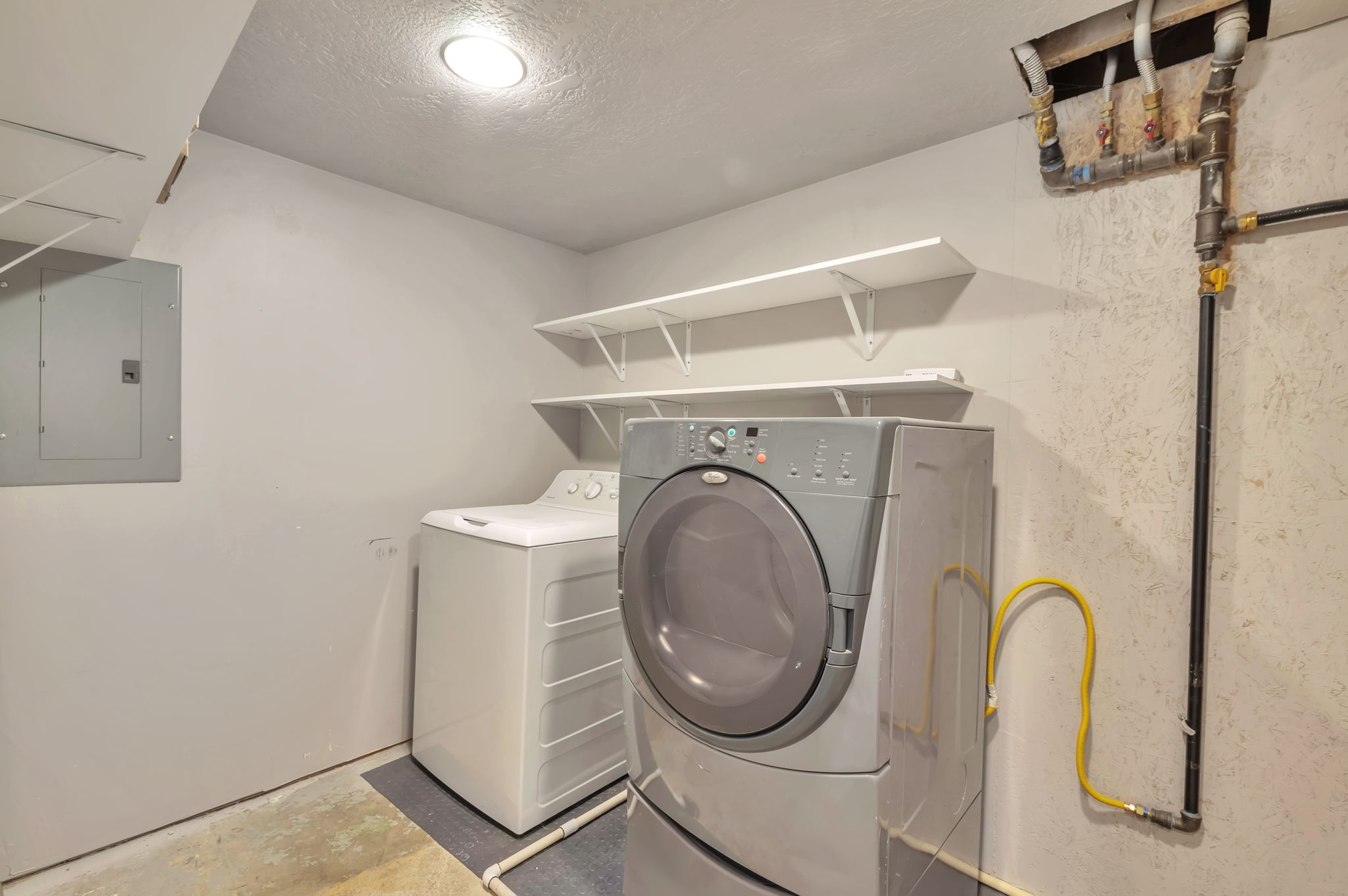 Laundry room with electric panel, concrete floors, washing machine and dryer, and a textured ceiling