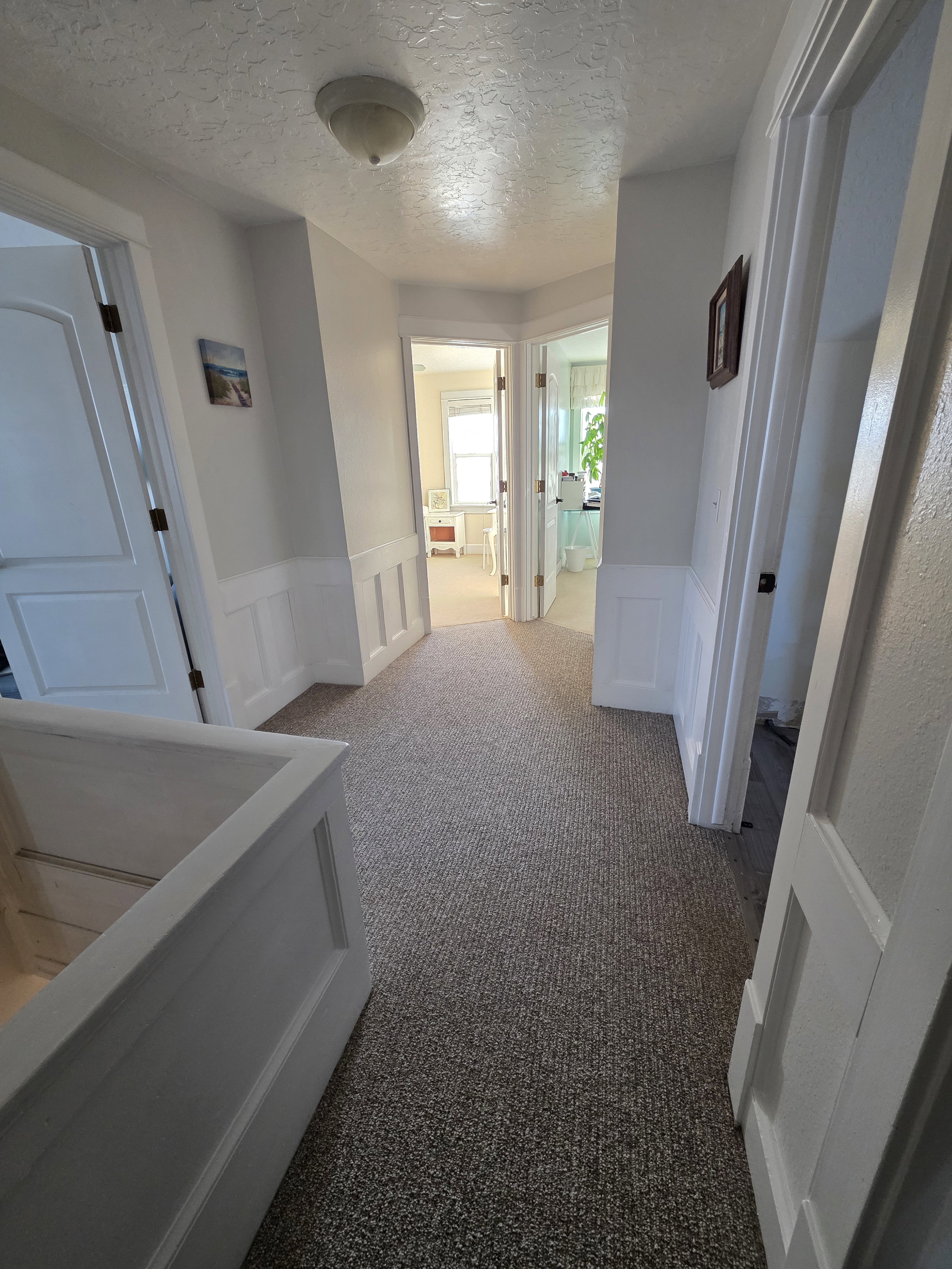 Hall with a decorative wall, a textured ceiling, wainscoting, and light colored carpet