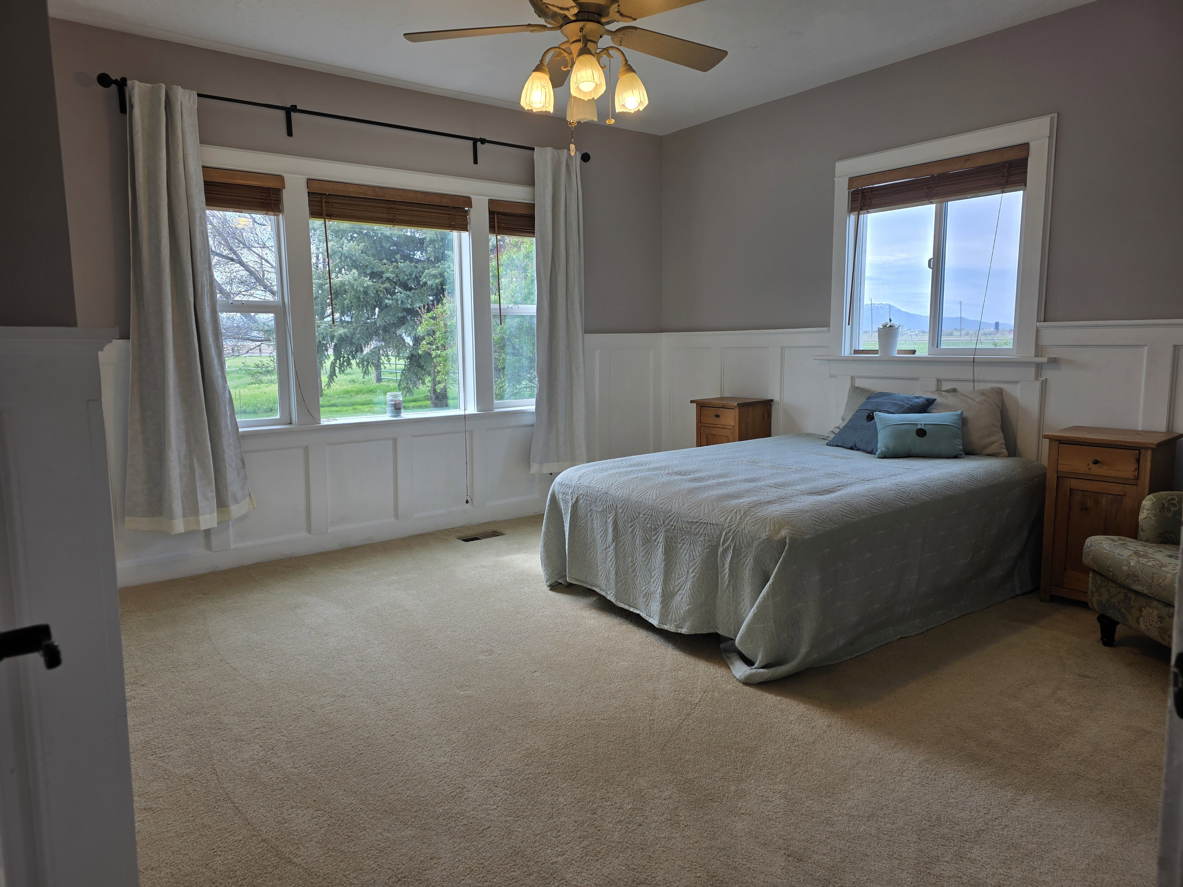 Bedroom featuring a decorative wall, wainscoting, ceiling fan, and light carpet
