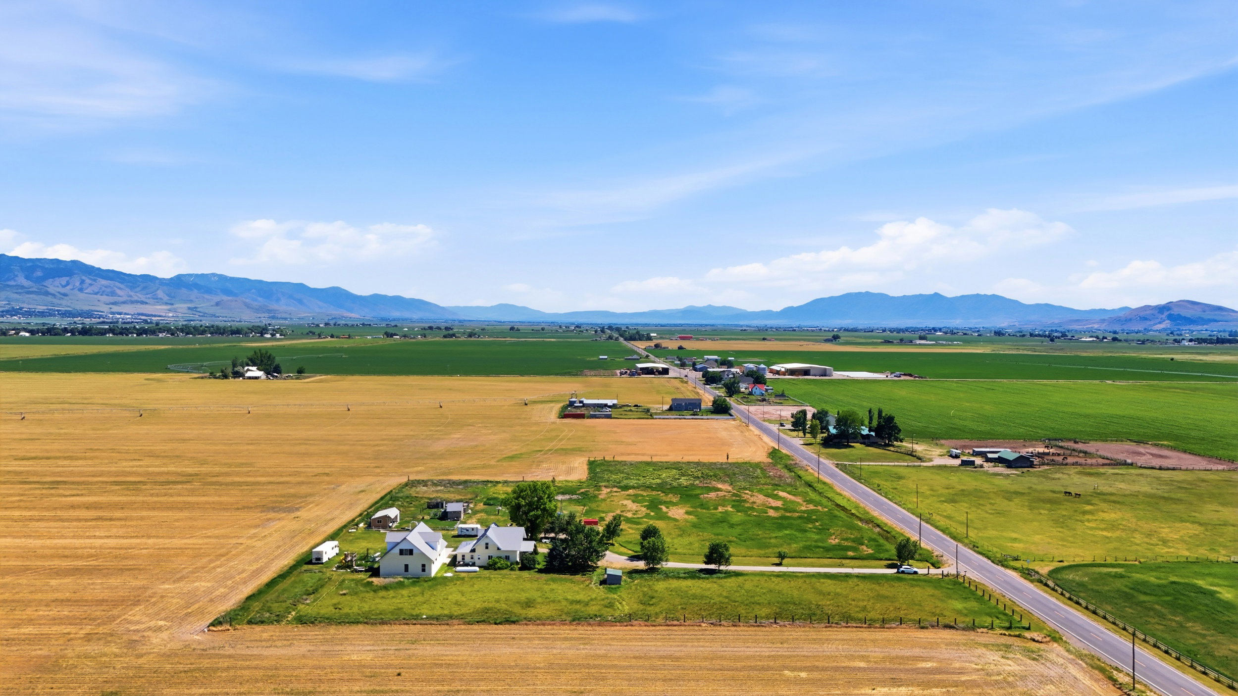 Expansive agricultural land featuring a primary residence with a white exterior, multiple outbuildings, and a paved road frontage