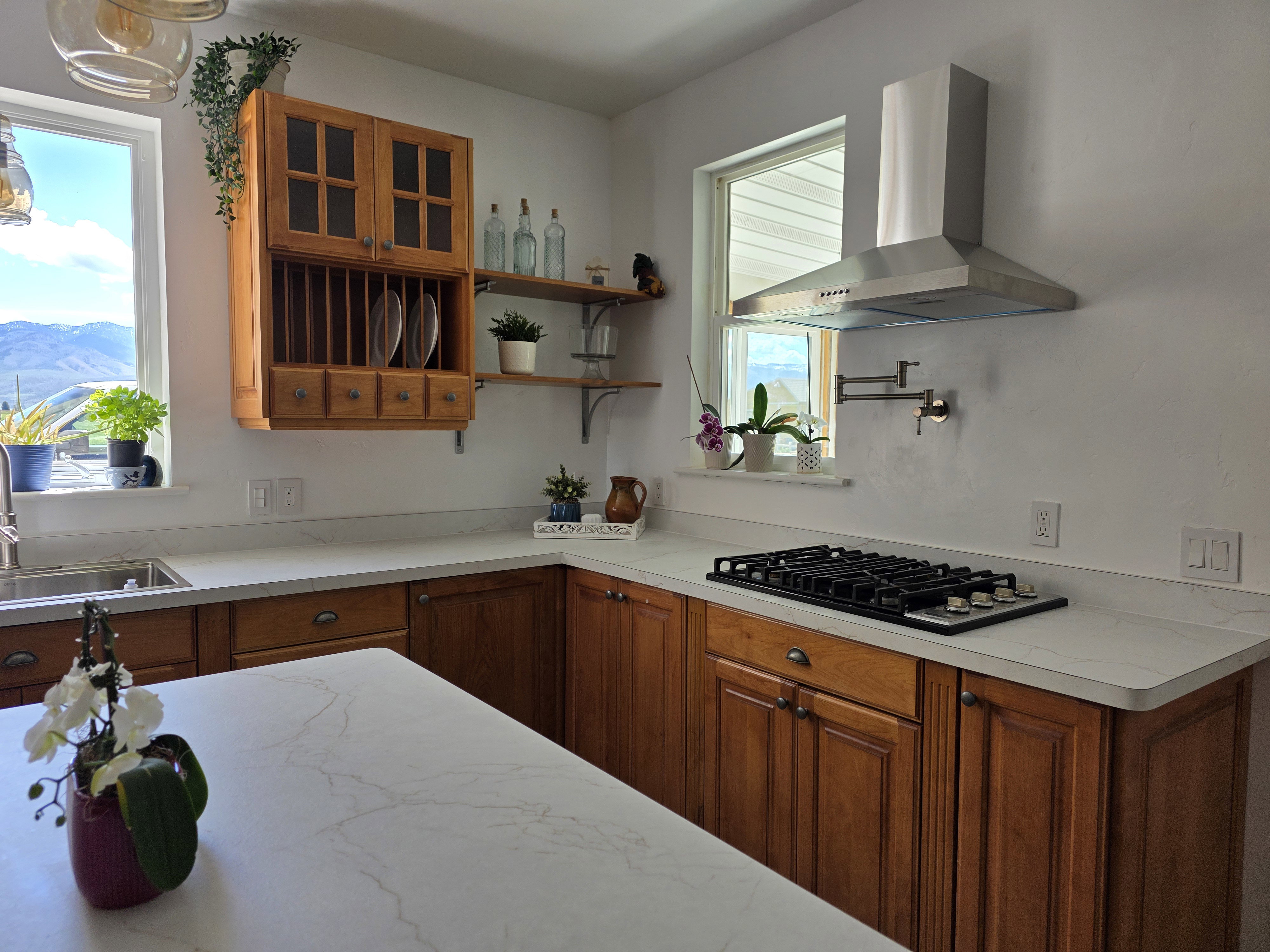 Kitchen featuring an integrated gas cooktop, stainless steel range hood, pot filler, wood-finish cabinetry, and solid surface countertops