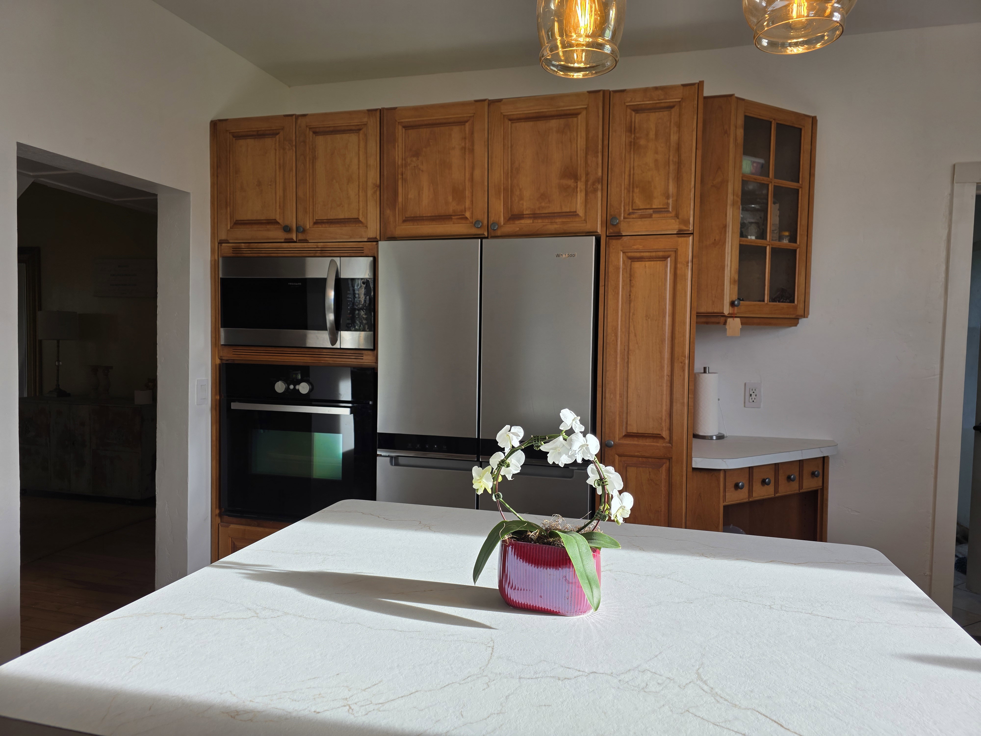 Kitchen featuring wood finish cabinetry, glass insert cabinets, stainless steel appliances, decorative light fixtures, and a center island