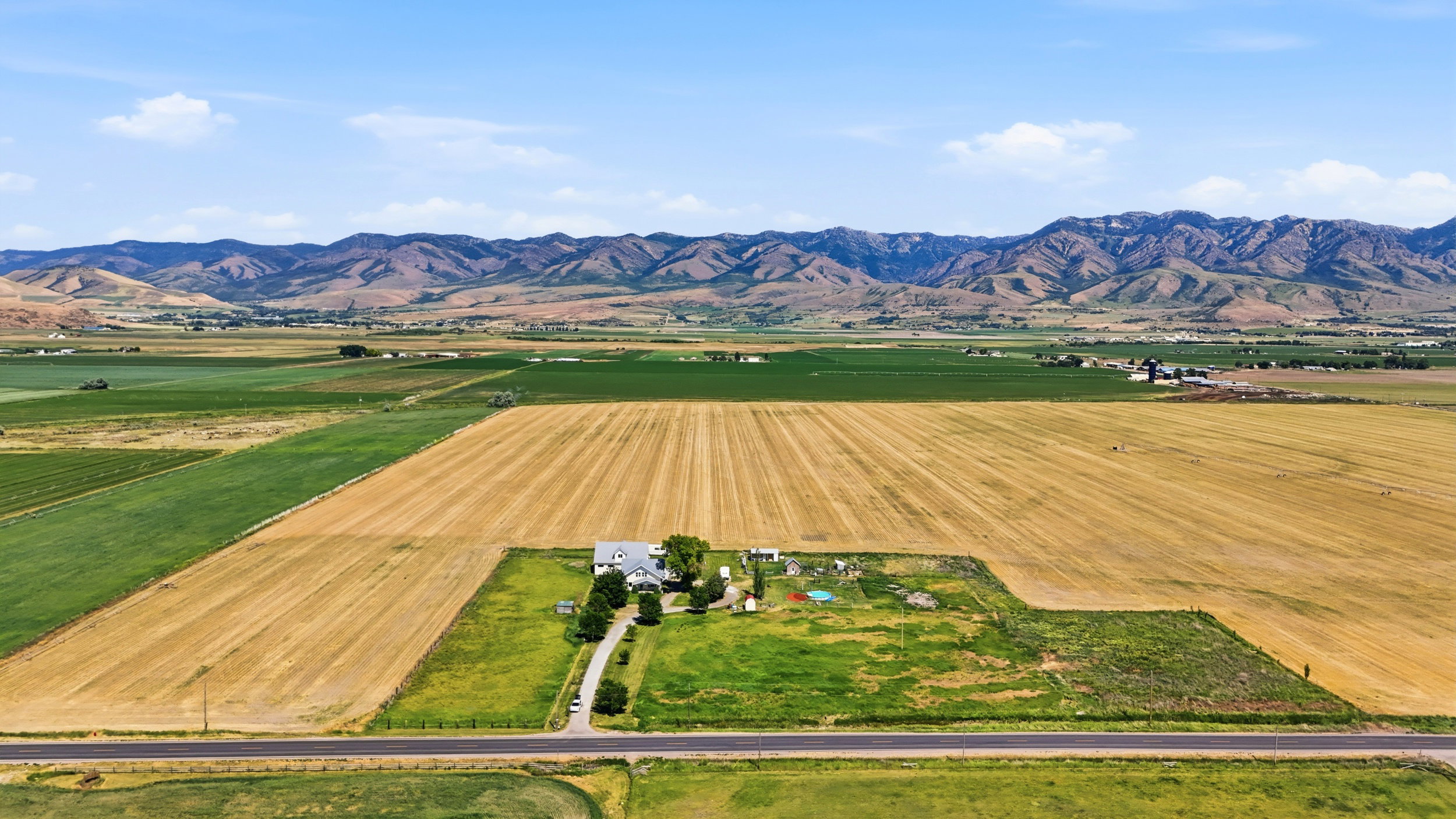 Expansive agricultural property featuring a two-story residence, multiple outbuildings, and a paved driveway