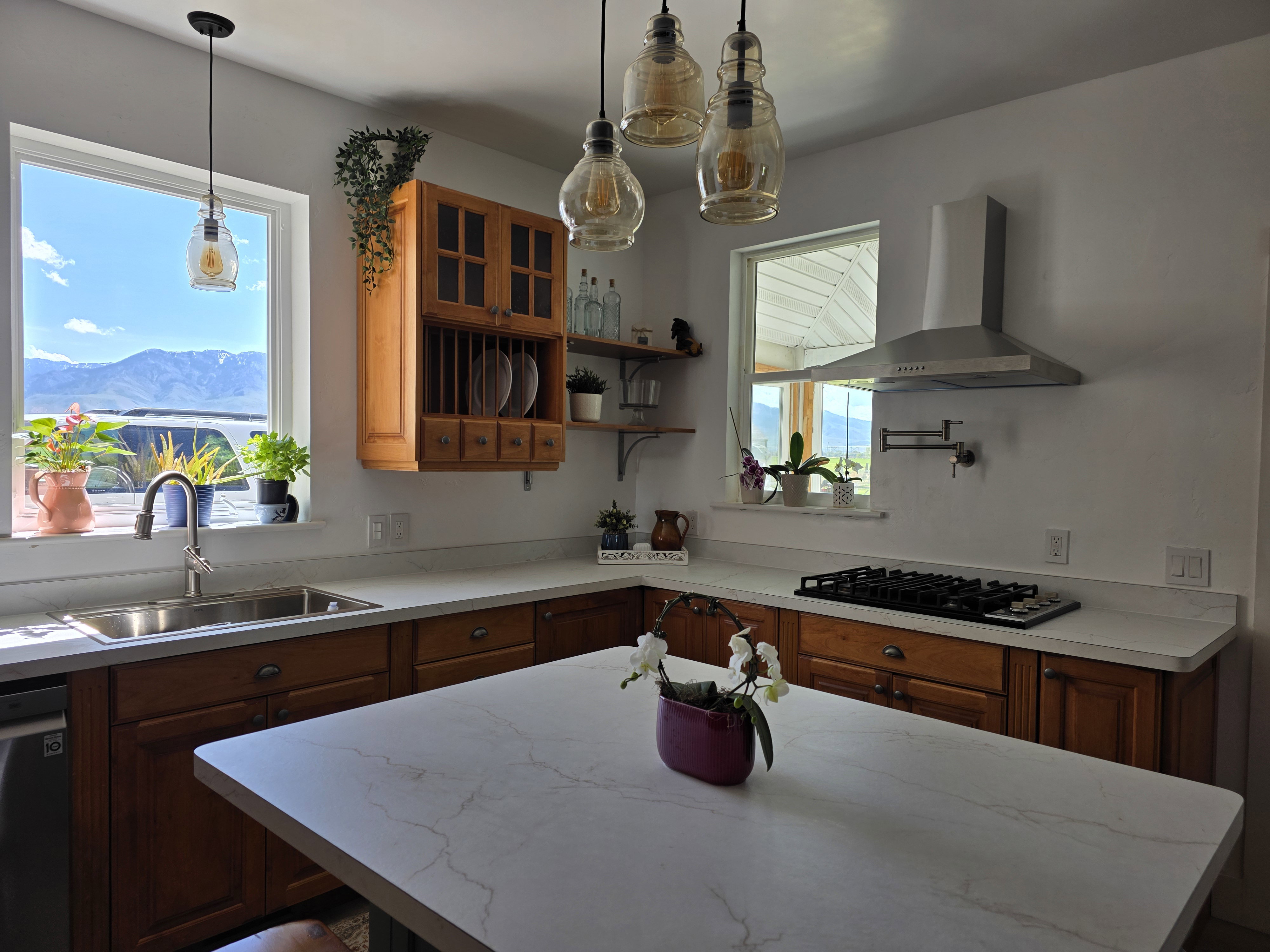 Kitchen featuring light wood cabinetry, white stone-finish countertops, stainless steel appliances, and a gas cooktop with a pot filler