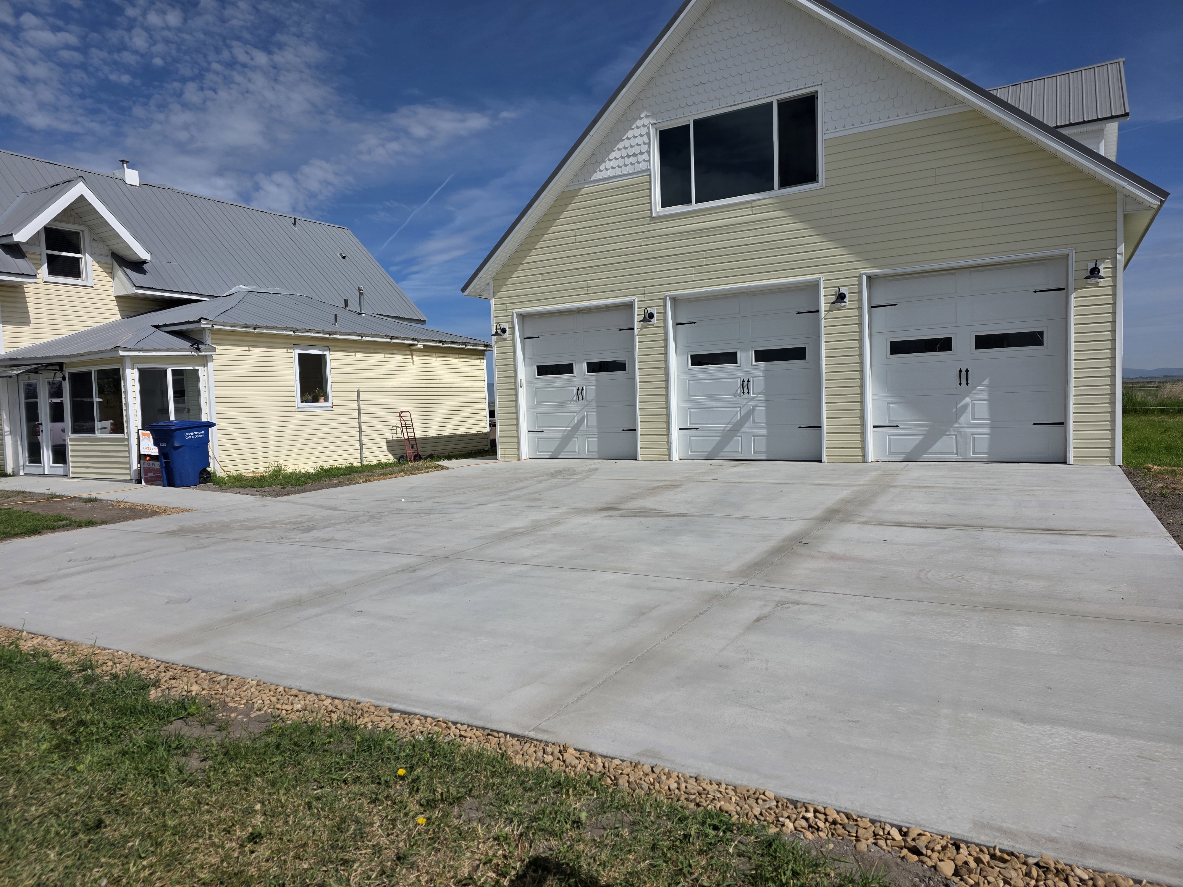 Three-car garage featuring white paneled doors with decorative hardware and transom windows, accompanied by a large paved concrete driveway