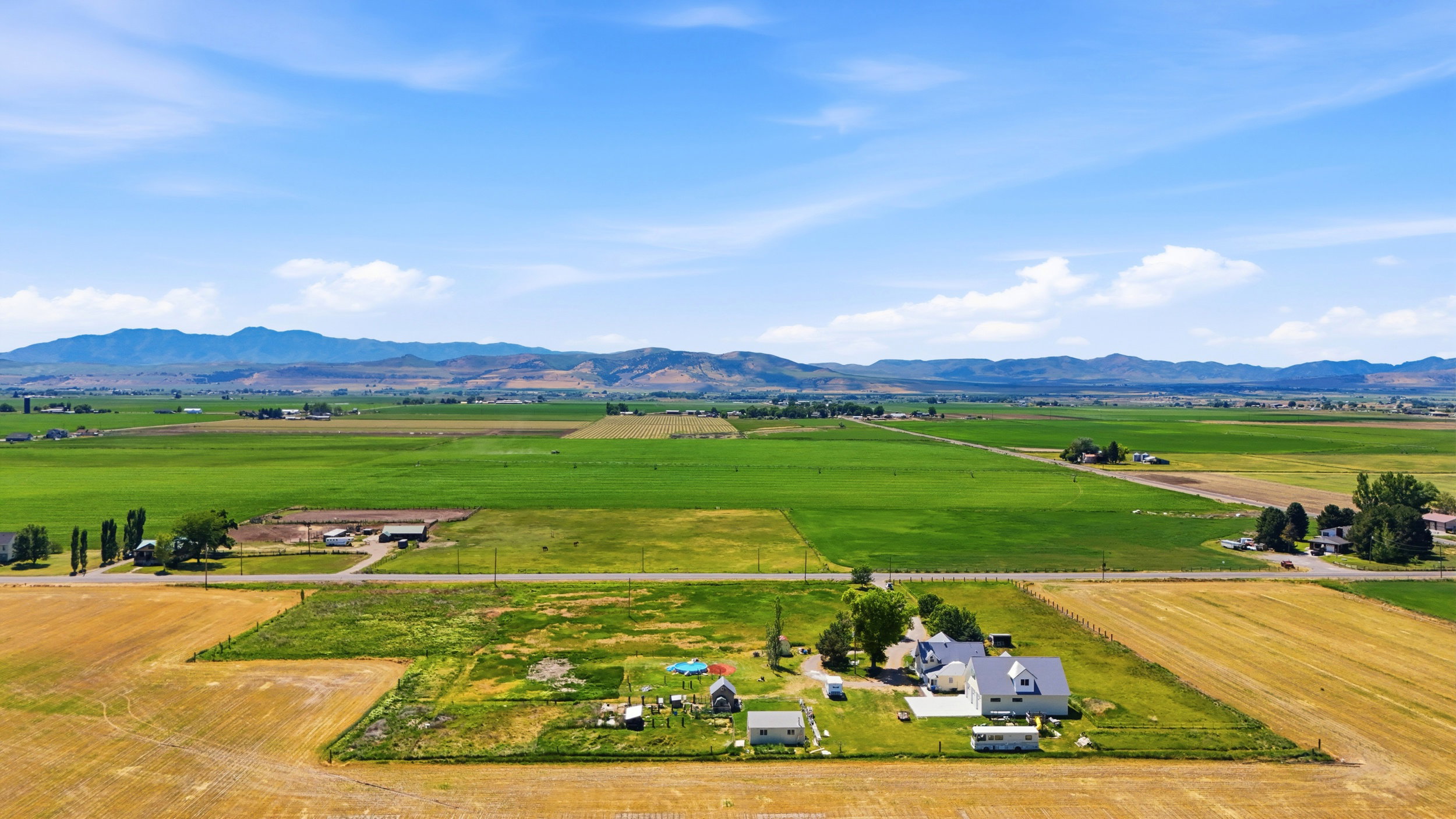 Expansive agricultural land featuring a primary residence with a white exterior and dark roof, multiple outbuildings, and cultivated fields
