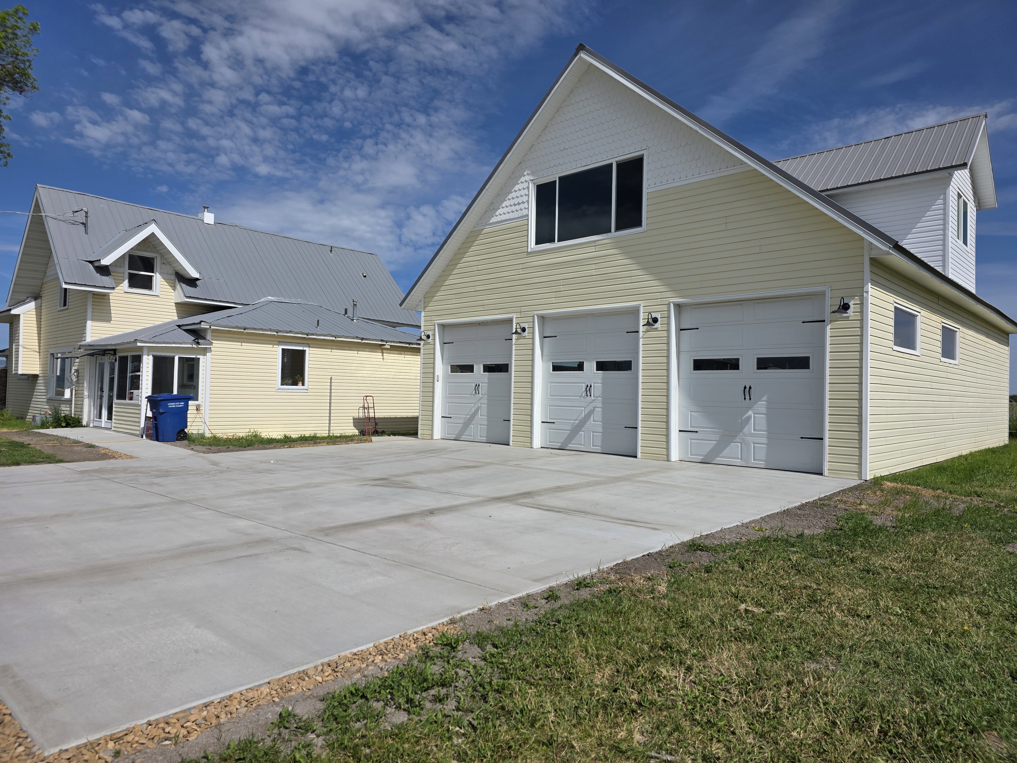 Detached multi-car garage with three overhead doors, yellow siding, and a metal roof