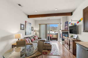 Living area featuring a glass covered fireplace, light wood-type flooring, beamed ceiling, recessed lighting, and a textured ceiling