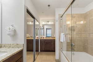 Full bath featuring two vanities, tiled shower / bath combo, and light tile patterned floors
