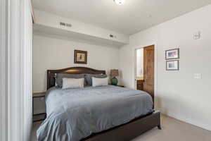 Bedroom with light carpet, connected bathroom, and a textured ceiling