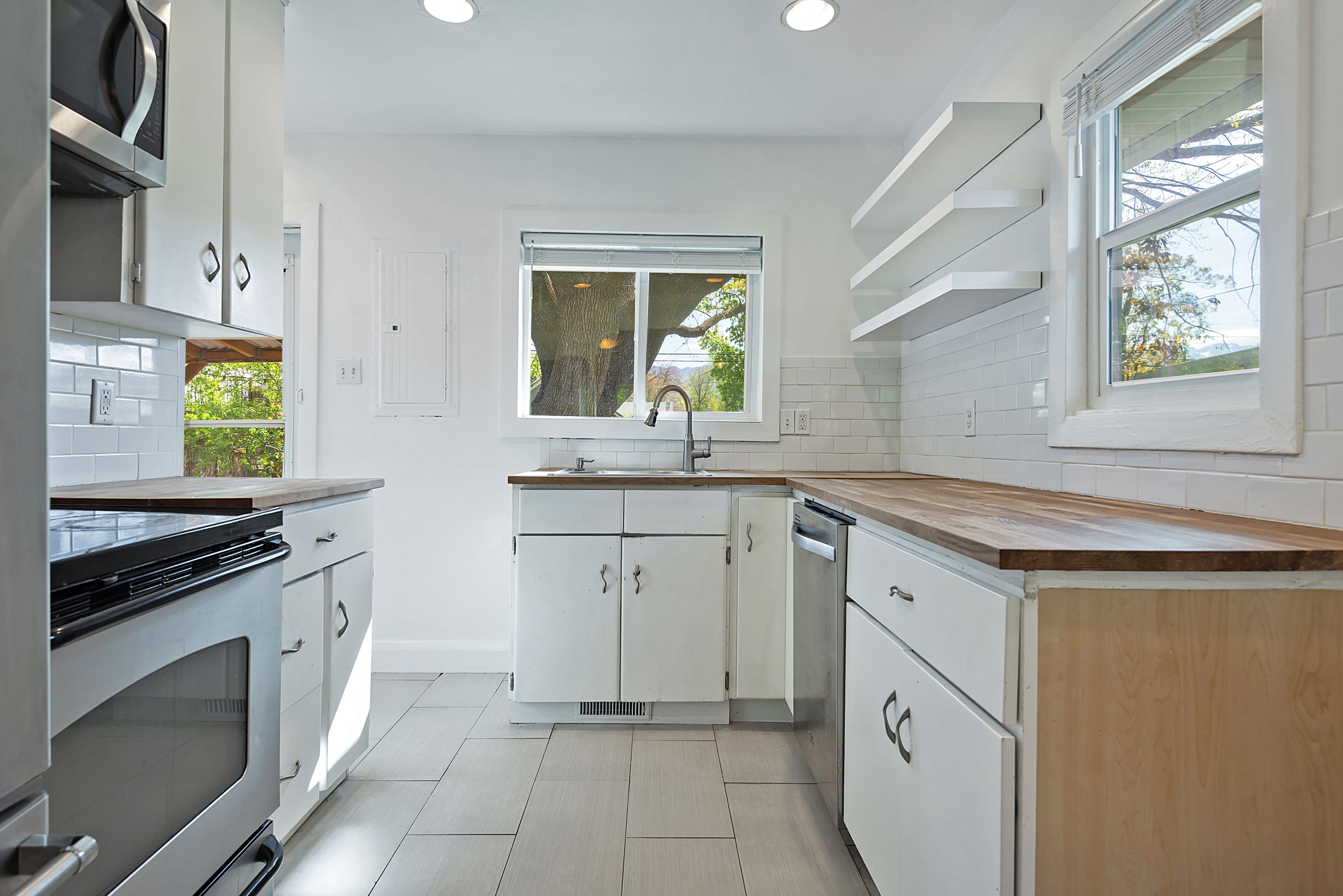 Kitchen with open shelves, tasteful backsplash, butcher block countertops, stainless steel appliances, and white cabinetry