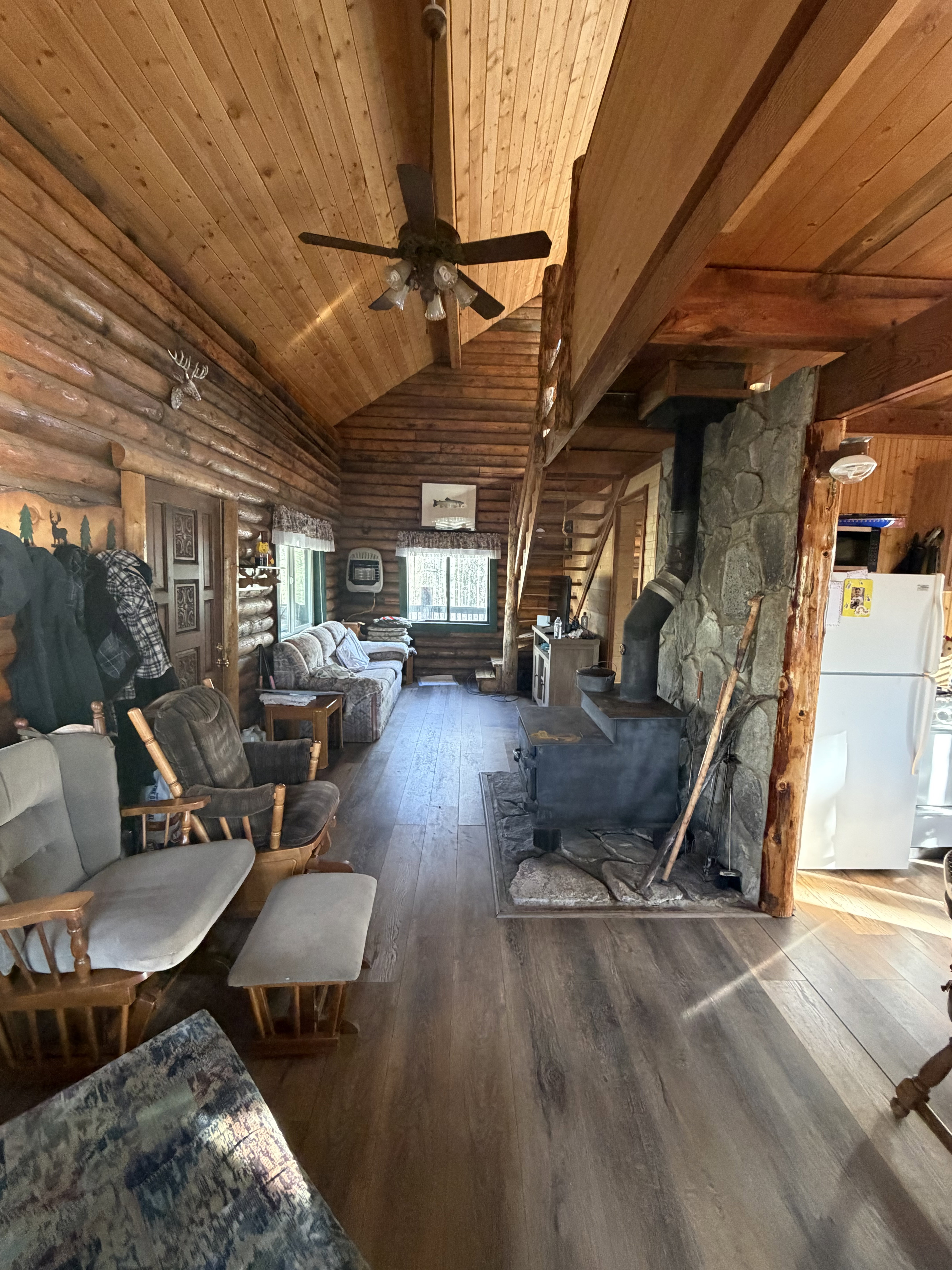 Living area with a wood stove, hardwood / wood-style floors, a vaulted wooden ceiling, a ceiling fan, and log walls