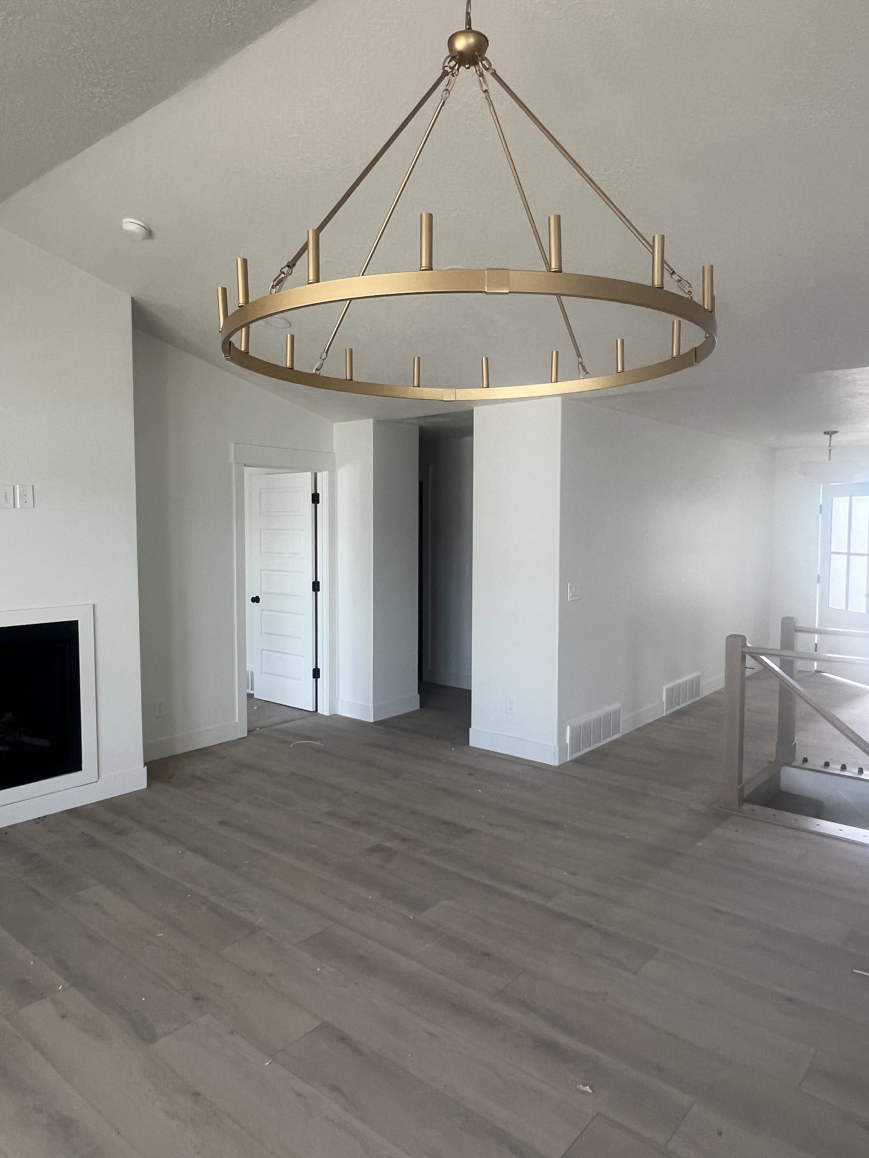 Spacious interior featuring a large gold-finish chandelier, light wood-finish flooring, a contemporary fireplace, white baseboards, and a modern stair railing