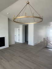 Spacious interior featuring a large gold-finish chandelier, light wood-finish flooring, a contemporary fireplace, white baseboards, and a modern stair railing