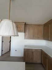 Kitchen featuring natural wood-finish cabinetry, light-toned countertops, recessed ceiling lighting, and a decorative pendant light fixture