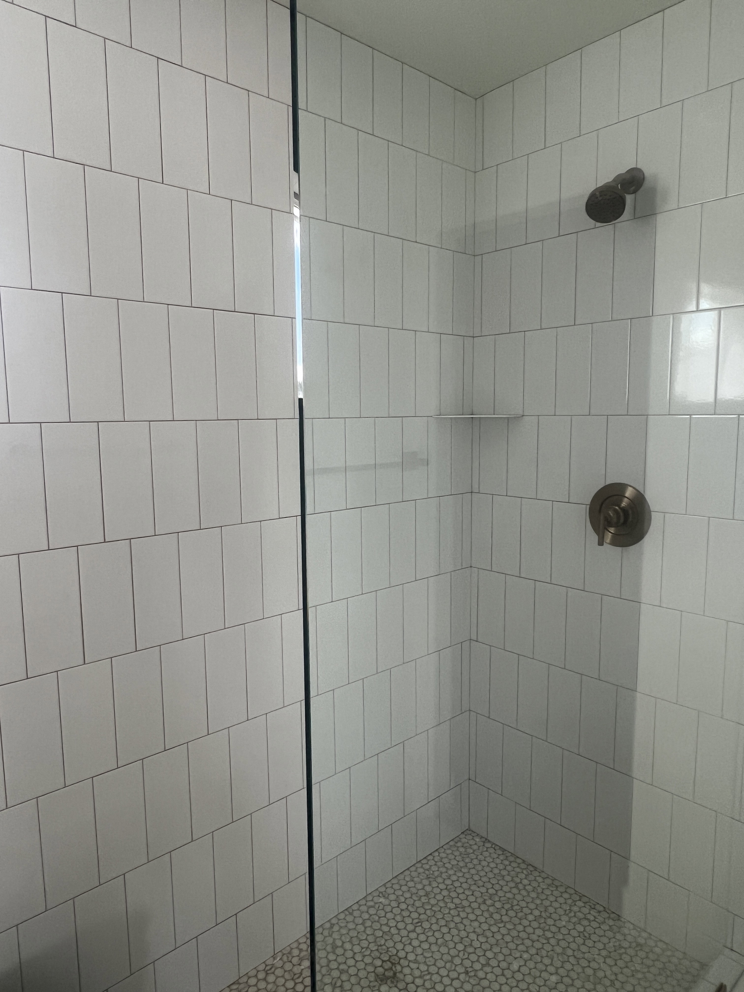 Shower enclosure featuring white vertical subway tile, glass shower panel, bronze shower fixtures, and a white penny tile shower pan