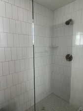 Shower enclosure featuring white vertical subway tile, glass shower panel, bronze shower fixtures, and a white penny tile shower pan