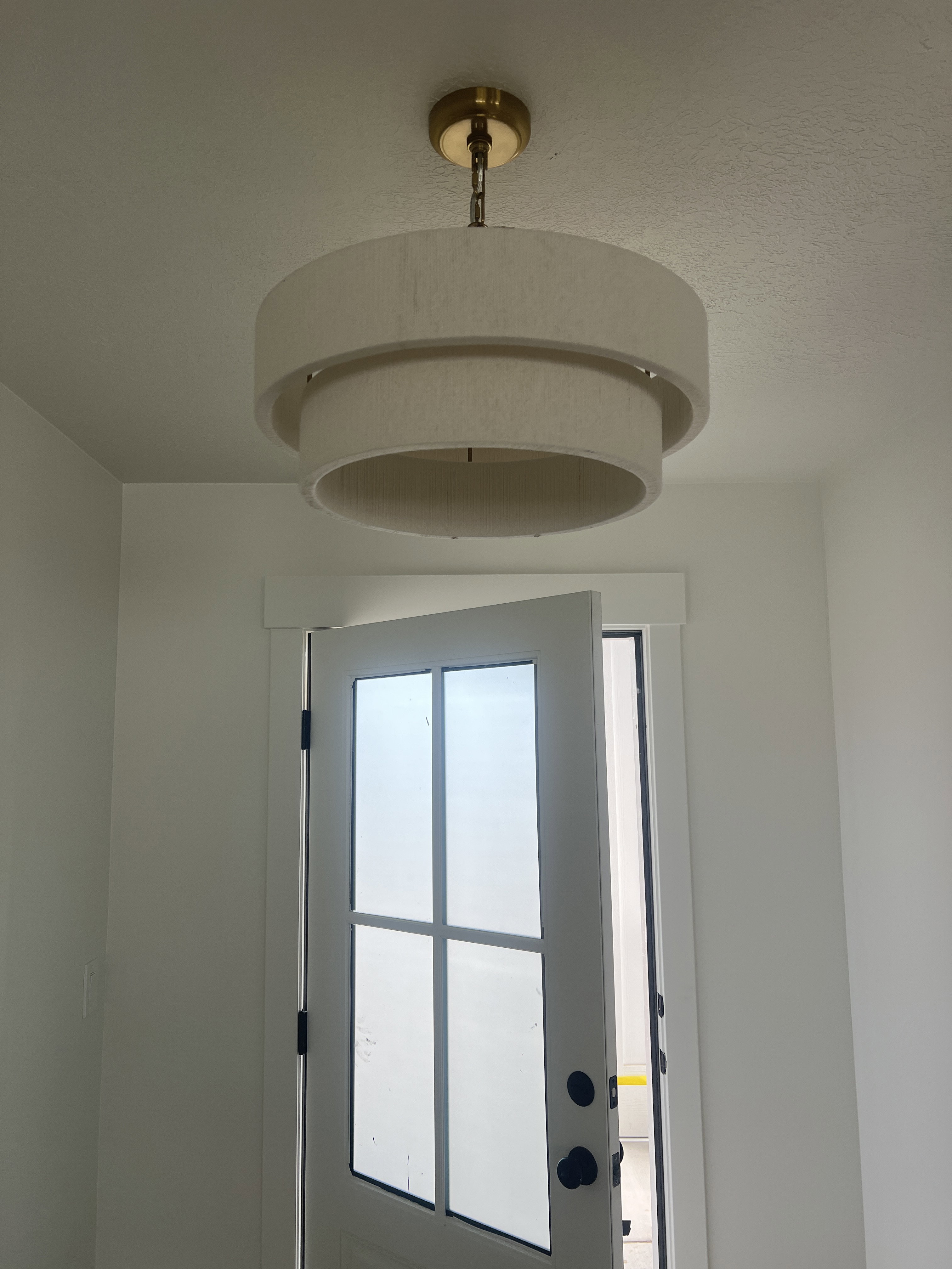 Layered drum pendant light with a brass-finish fixture, white trim, and a paneled door with divided lites and matte black hardware