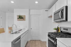Kitchen featuring stainless steel appliances, white cabinets, a peninsula, light stone counters, and recessed lighting