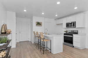 Kitchen with stainless steel appliances, a kitchen bar, white cabinets, light wood-style floors, and recessed lighting