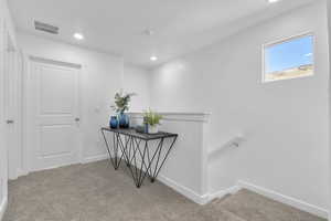 Hall with an upstairs landing, light colored carpet, and recessed lighting