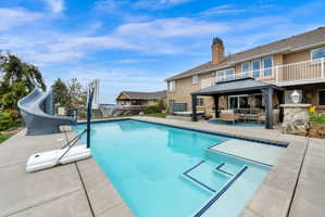 View of pool featuring patio surround, a water slide, outdoor lounge area, and a gazebo