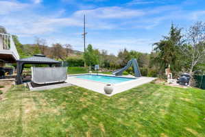 Swimming pool featuring a water slide, a patio area, a gazebo, and a lawn